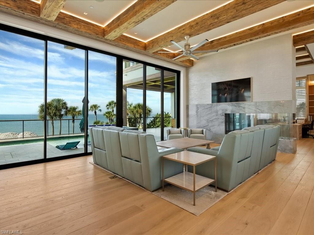 Living room with exposed wood beams, a marble fireplace, and ocean views through floor-to-ceiling glass doors.