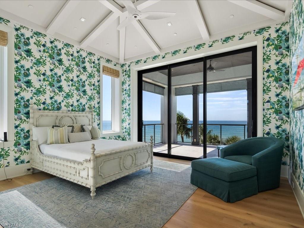 Bedroom with floral wallpaper, ornate white bed, and ocean view through sliding glass doors.