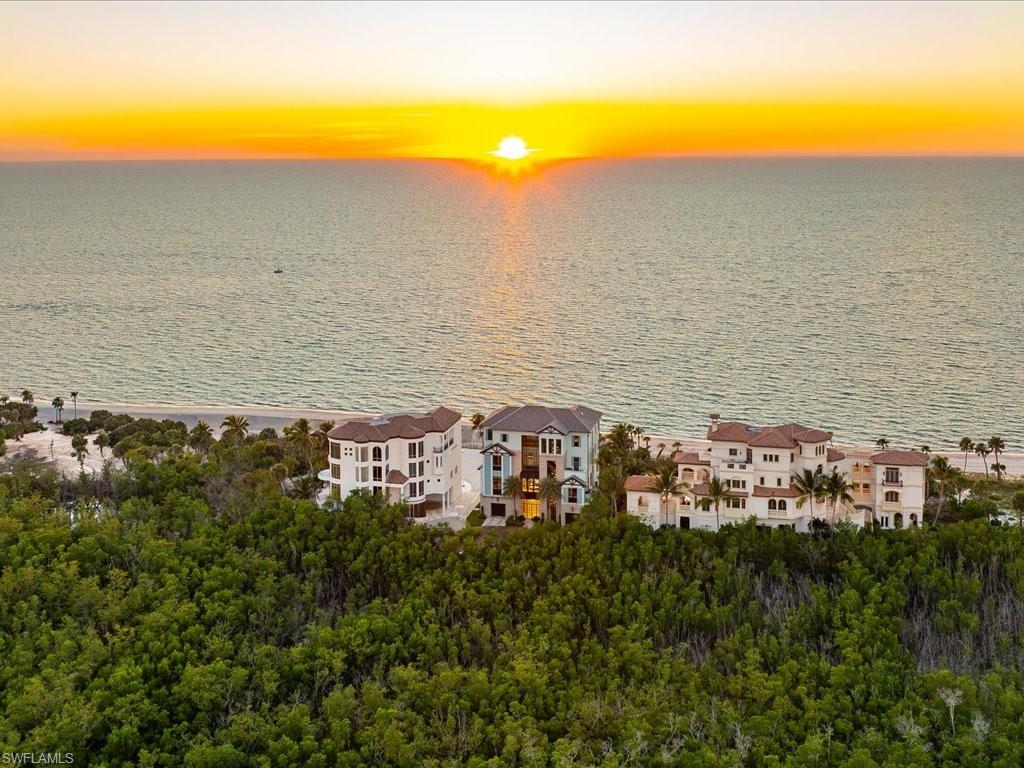 Aerial view of beachfront homes beside the Gulf at sunset, with the sun reflecting on the water.