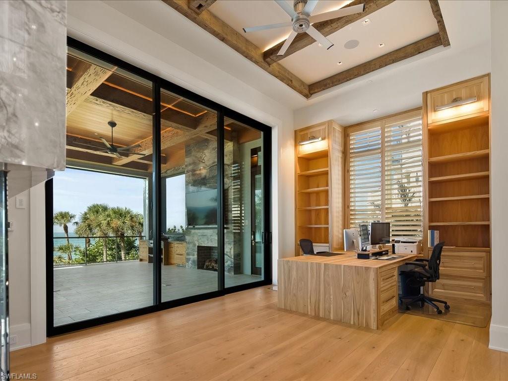 Home office with built-in wood shelving and desk overlooking a terrace and water.