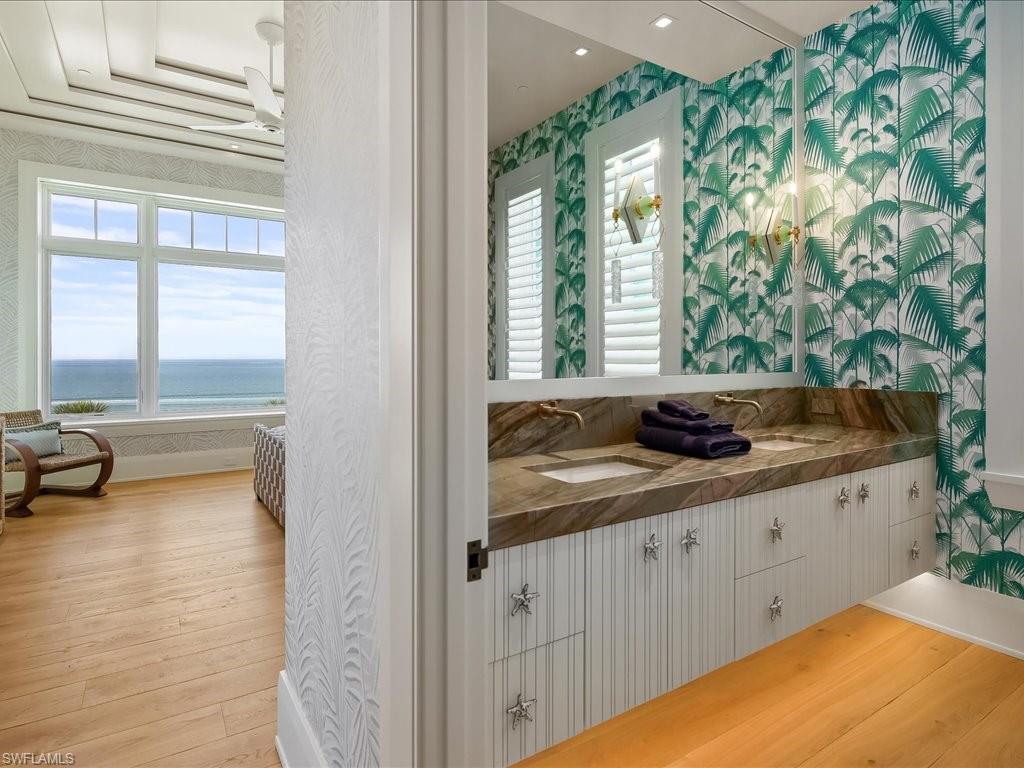 Bathroom vanity with palm-patterned wallpaper, beside a bedroom with an ocean-view window.
