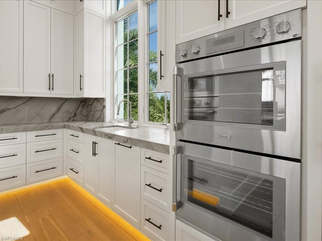 Kitchen with white shaker cabinets, veined stone counters, double oven, and a window overlooking palms.