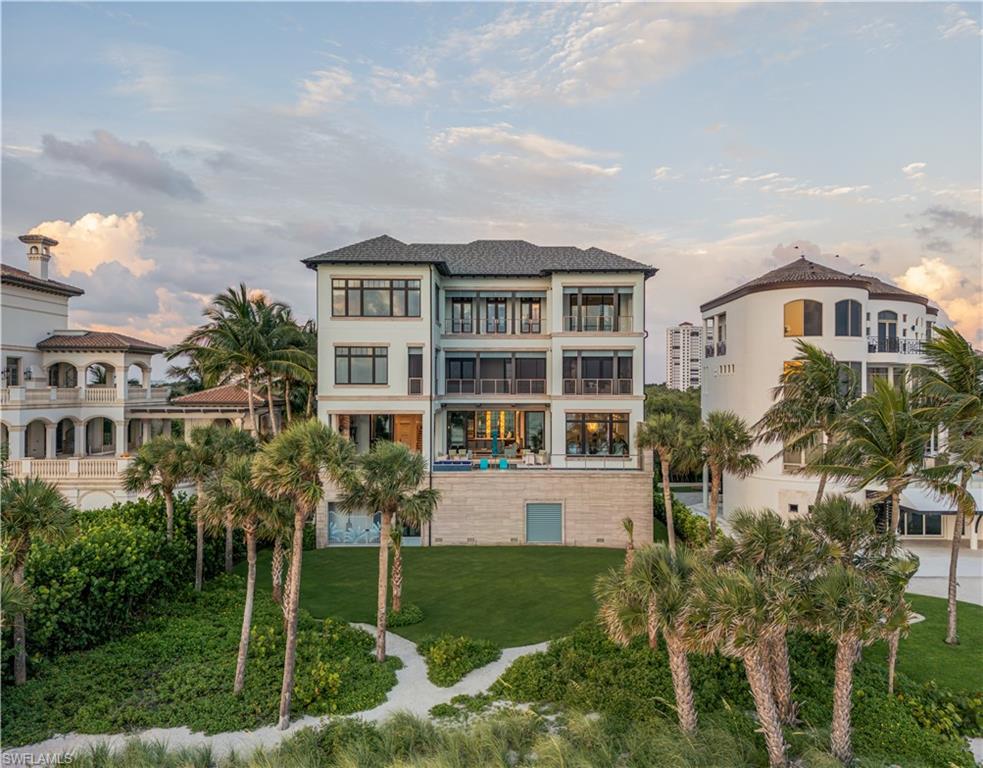Contemporary coastal home with balconies, a stone lower level, palm trees, and landscaped grounds.