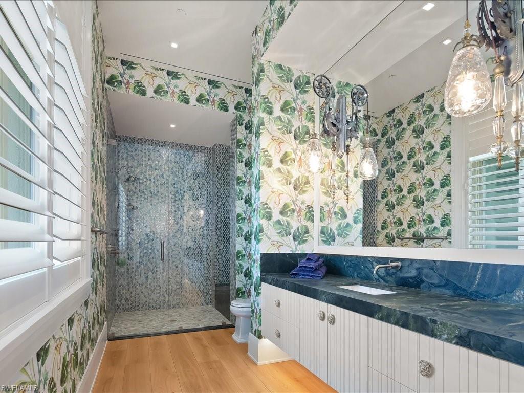 Bathroom with a mosaic-tile shower, dark blue double vanity, and leafy botanical wallpaper.