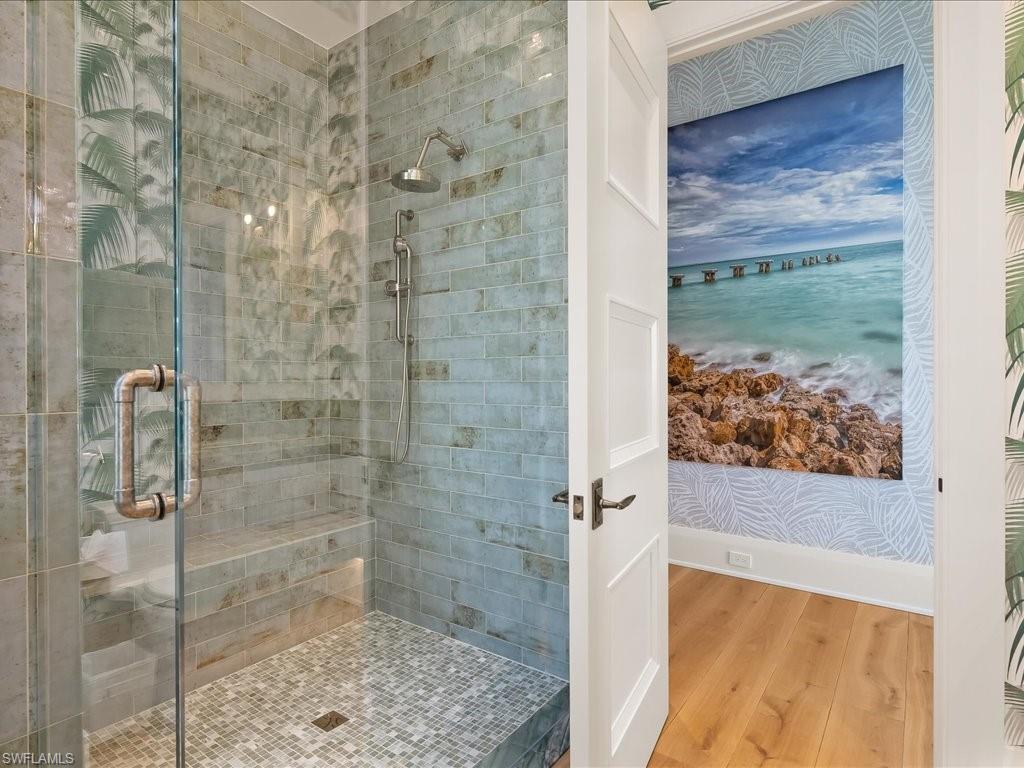 Walk-in shower with pale blue-green tile, a built-in bench, and a mosaic floor beside coastal artwork.