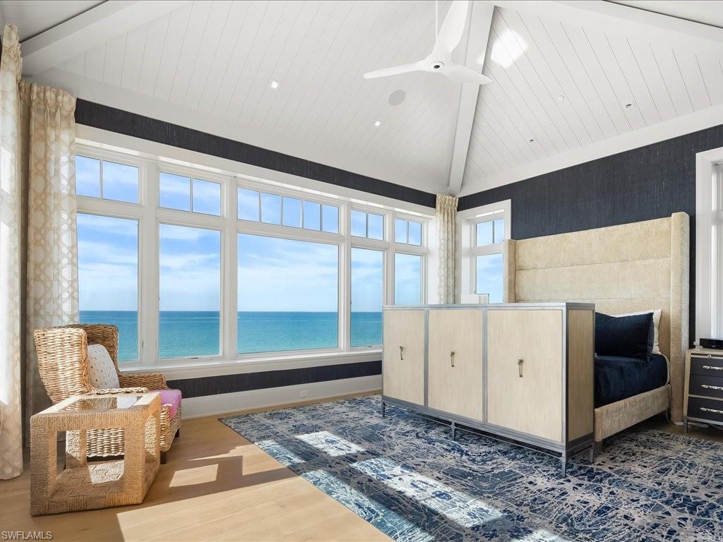 Ocean-facing bedroom with a vaulted white ceiling, expansive windows, and a blue patterned rug.