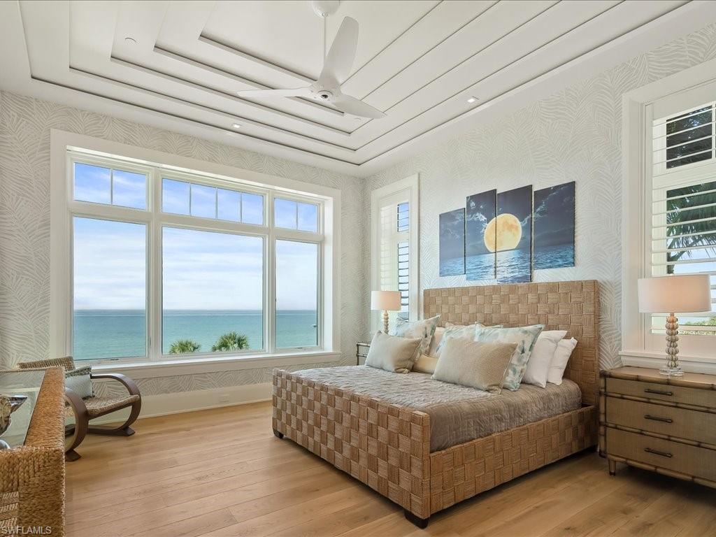 Oceanfront bedroom with a woven bed, tray ceiling, and large windows overlooking the water.