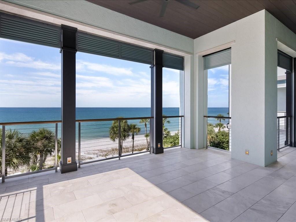 Covered tiled balcony overlooking the beach and ocean, with dark columns and a glass railing.