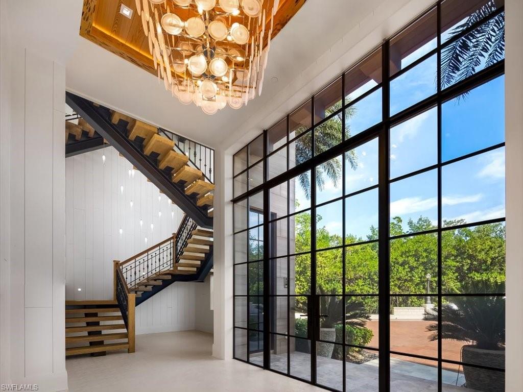 Modern entryway with a dramatic staircase, floor-to-ceiling windows, and a cascading glass chandelier.