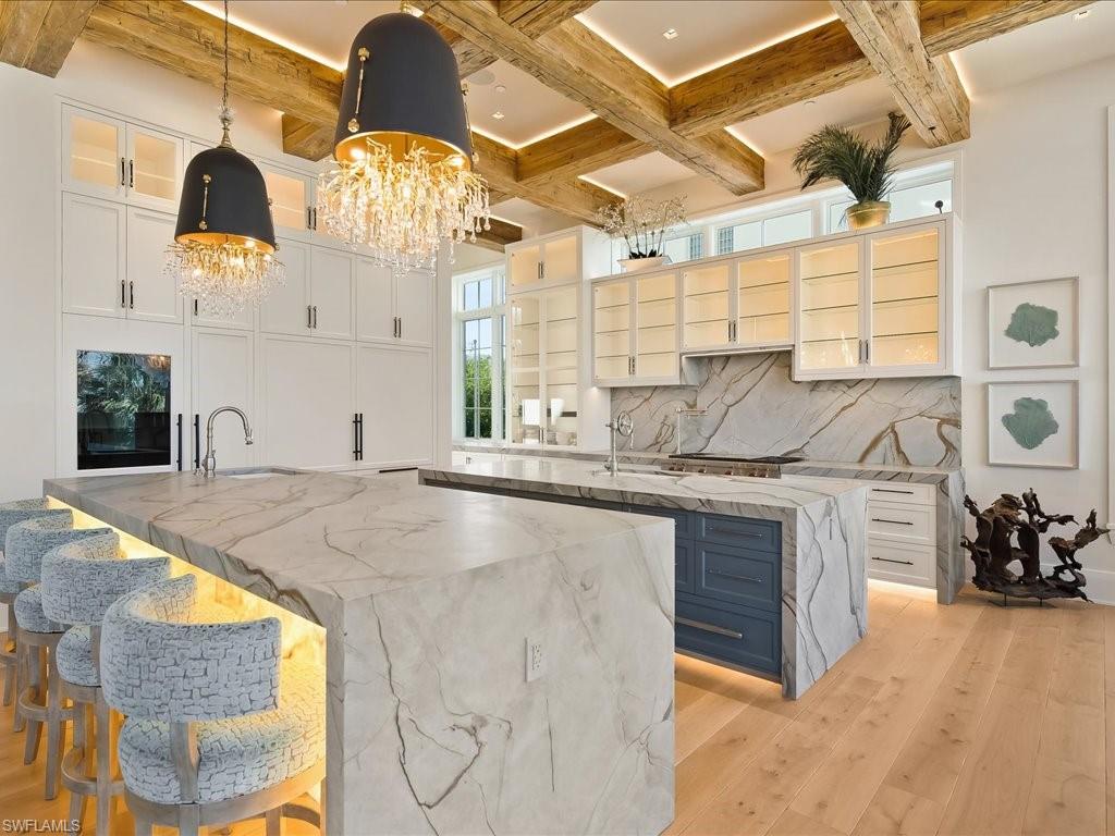 Luxury kitchen with a veined marble island, blue bar stools, and exposed wood ceiling beams.