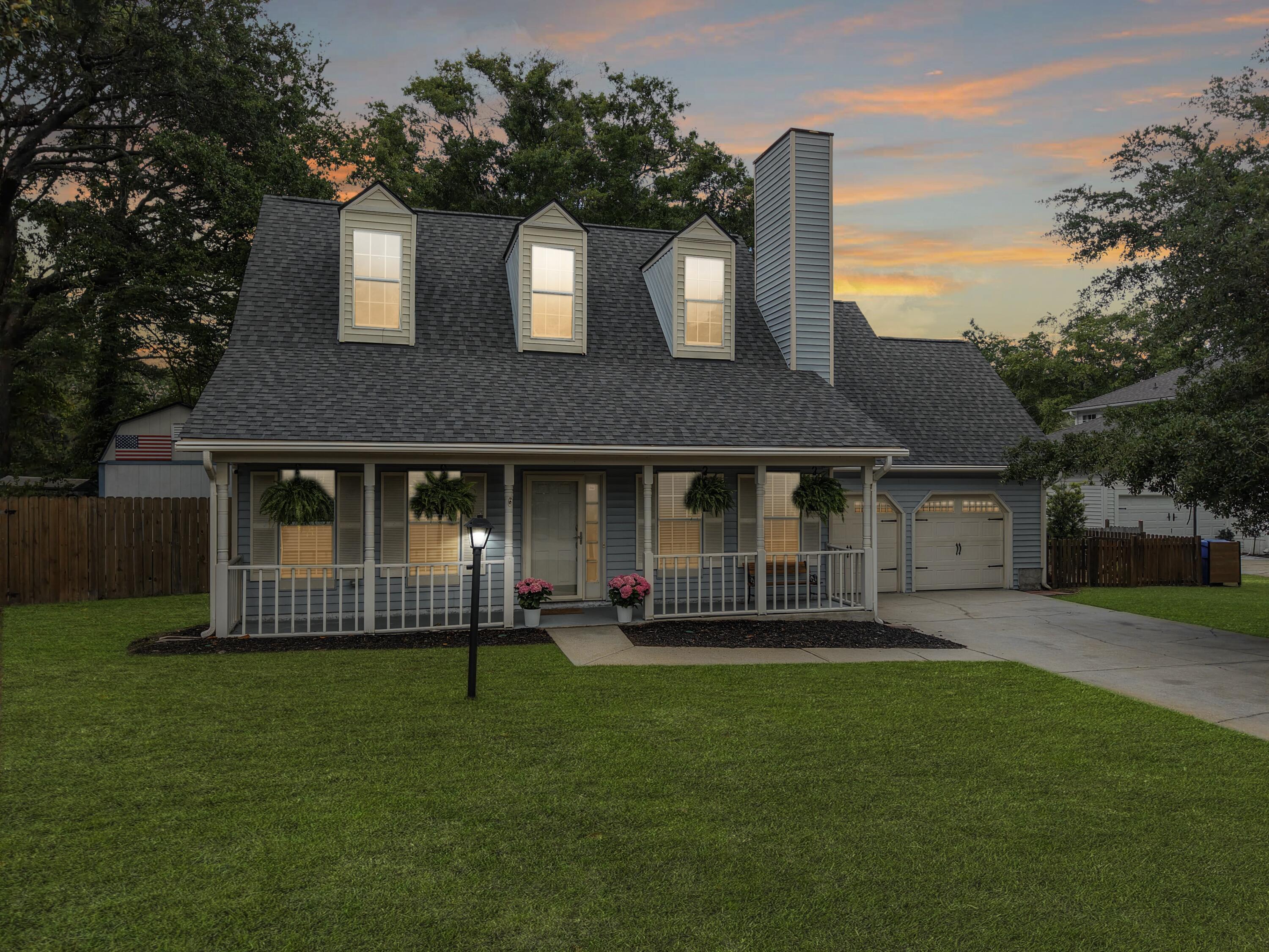 Gray two-story house with illuminated dormers, a covered porch, and broad lawn at dusk.