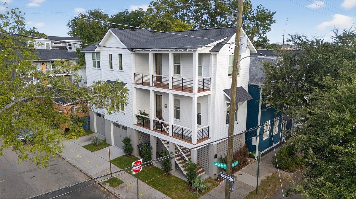 White multi-story home with stacked porches and black railings on a tree-lined corner lot.