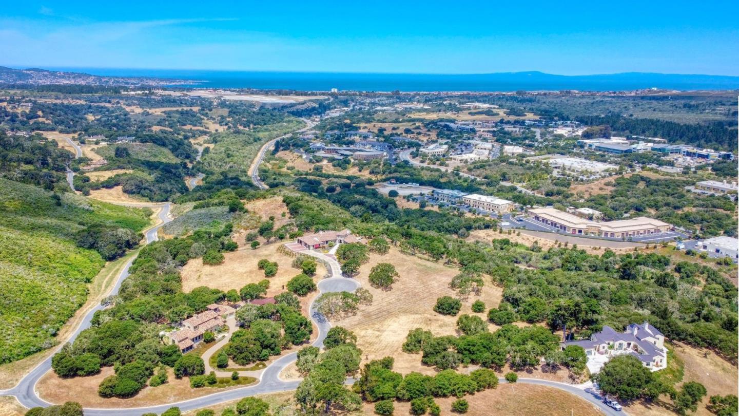 Aerial view of homes and winding roads, with wooded hills and the ocean in the distance.