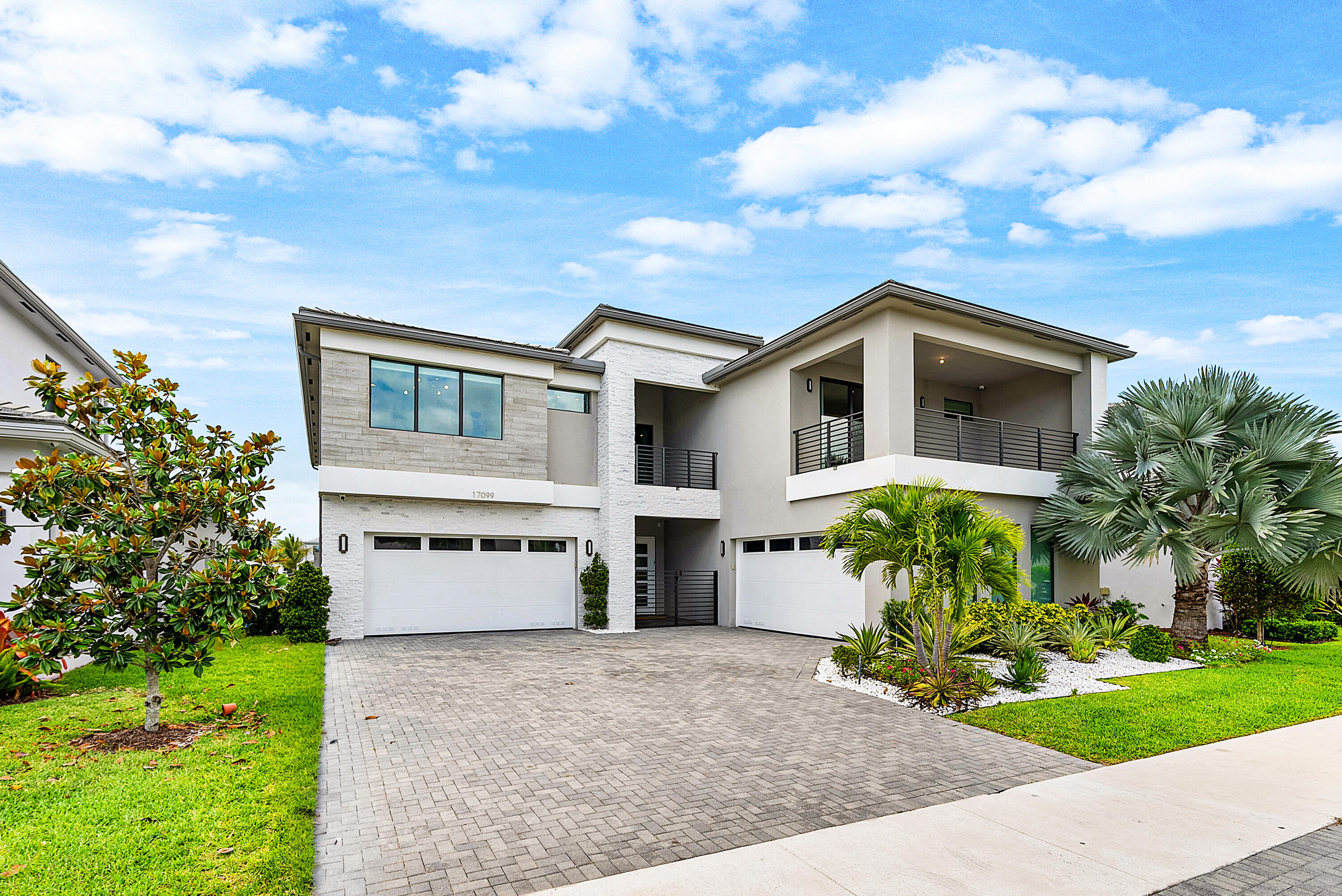 Modern two-story white home with covered balconies, two garages, and tropical landscaping.