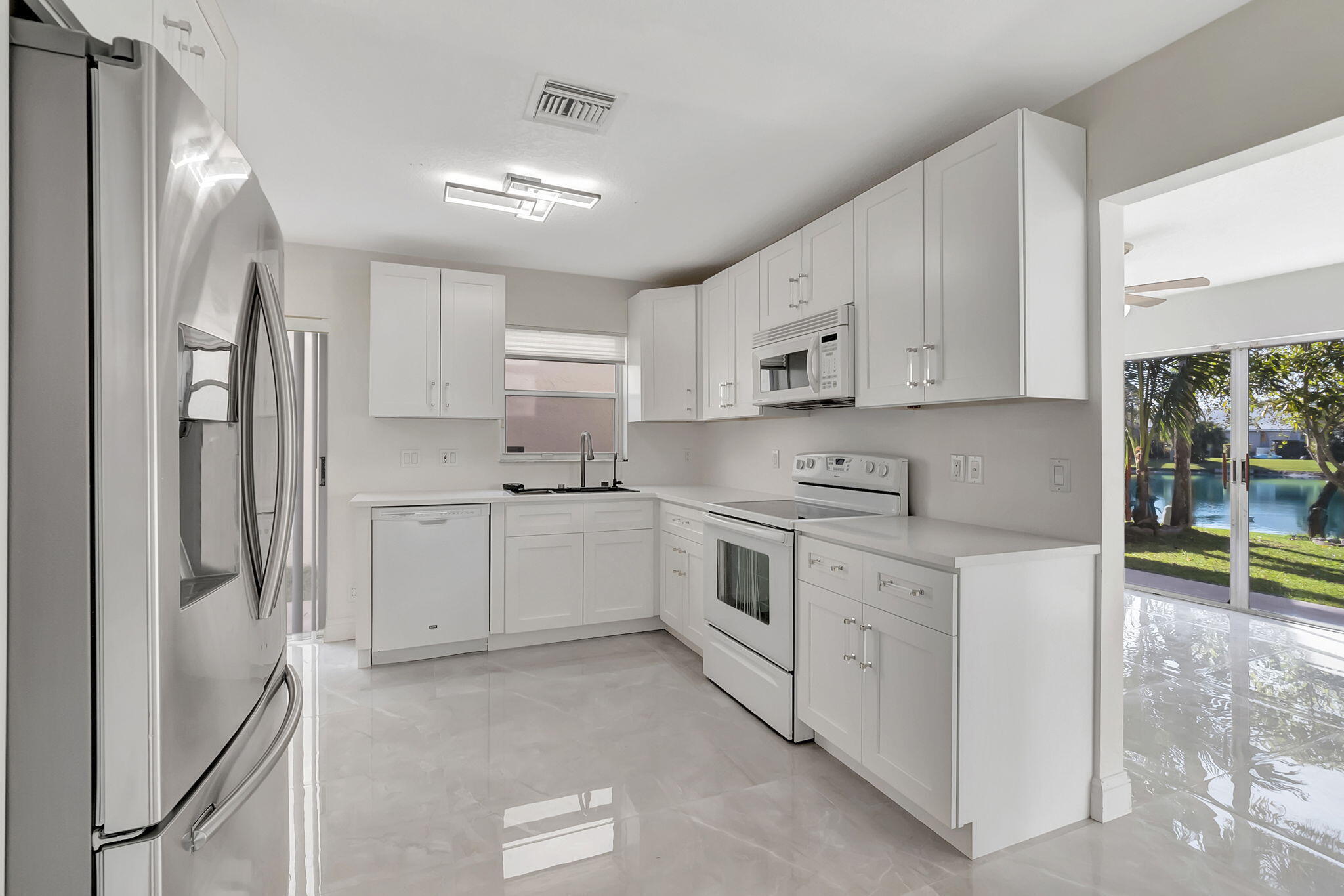 White kitchen with stainless steel appliances and a pool view through sliding glass doors.
