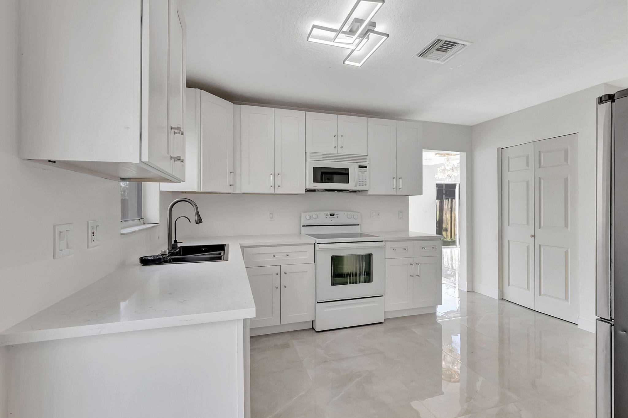 Bright white kitchen with shaker cabinets, a black sink, white range, and glossy tile floors.