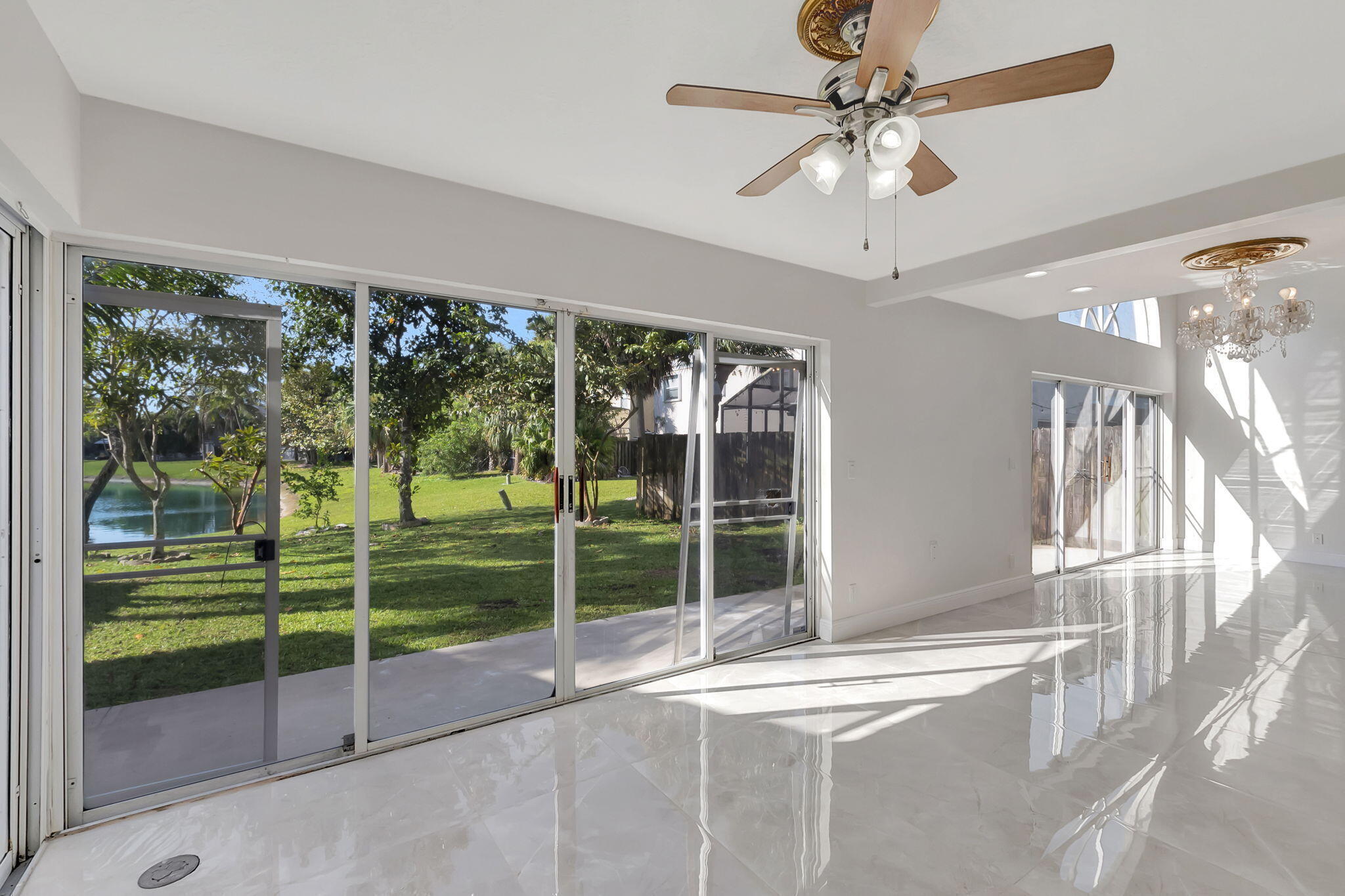Vacant living and dining area with glossy tile floors and sliding doors overlooking a grassy yard and water.