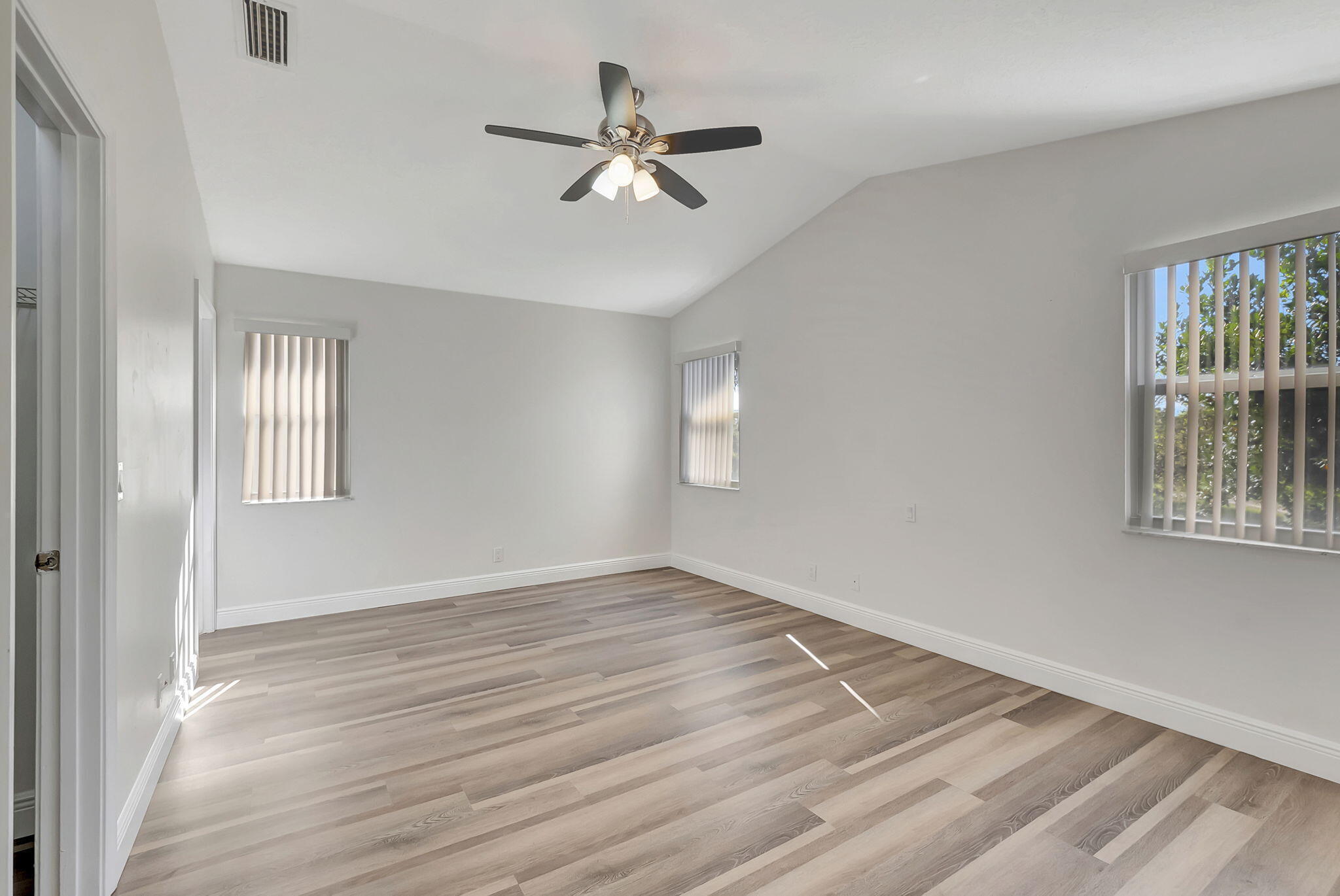 Empty bedroom with gray plank flooring, vertical blinds, and a ceiling fan with lights.