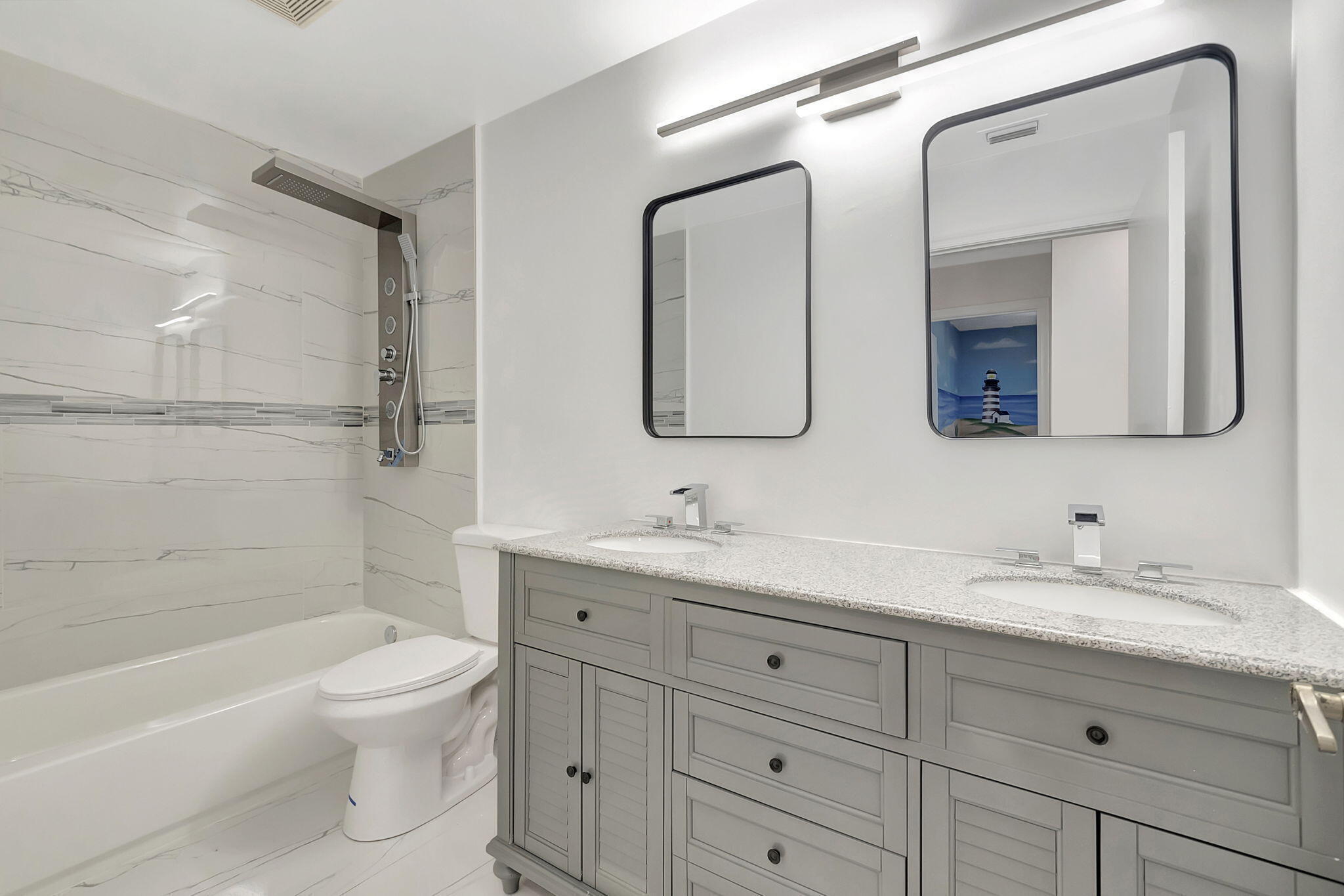 Bathroom with a gray double vanity, black-framed mirrors, and a marble-look tiled tub and shower.