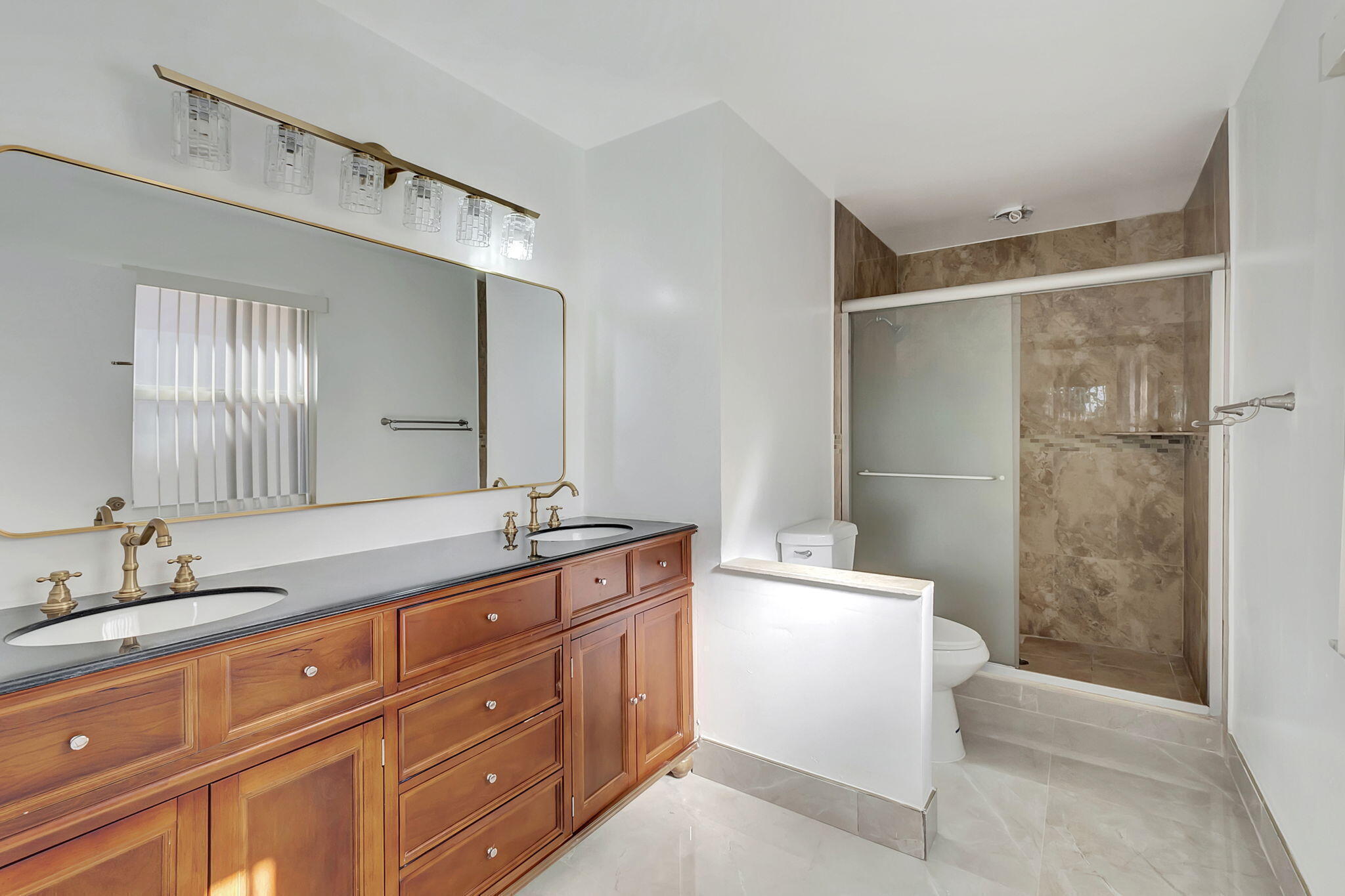 Bathroom with a long wooden double vanity and a glass-enclosed stone-tile shower.