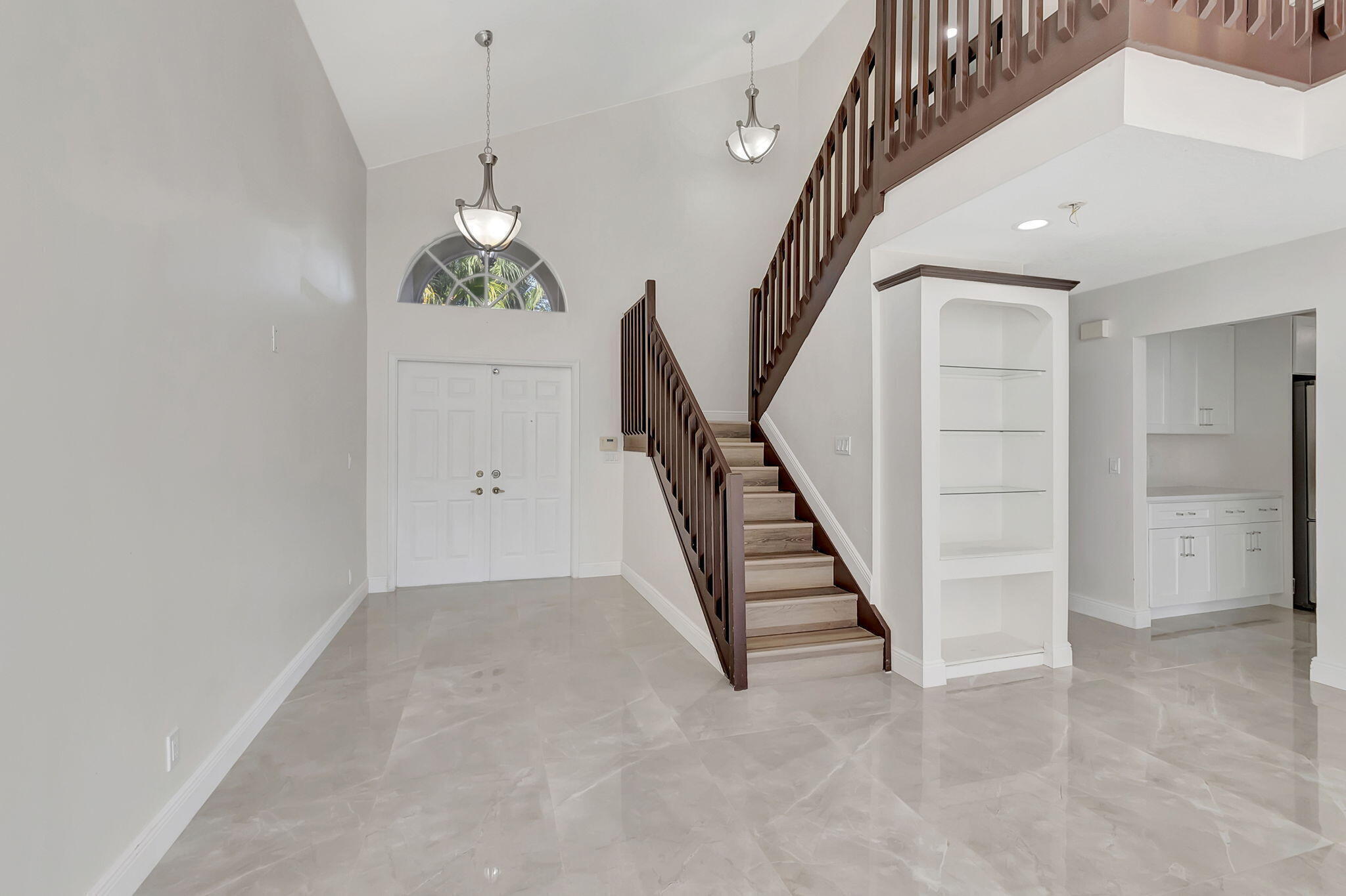 Two-story foyer with a dark wood staircase, arched window, glossy tile floor, and built-in shelves.
