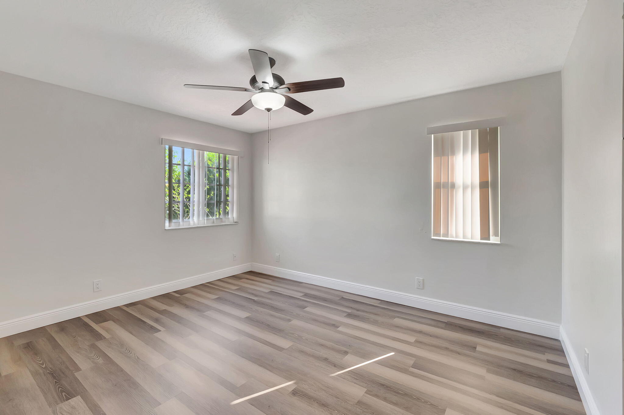 Empty room with wood-look plank flooring, two windows, and a ceiling fan with light.