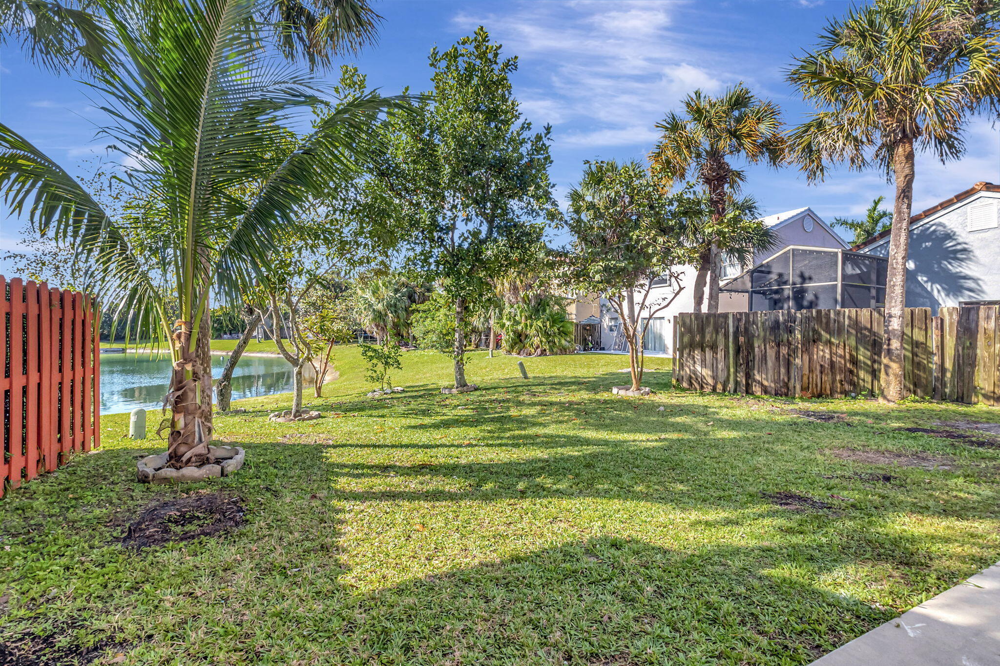 Backyard with a lake, palm trees, and screened patio behind the home.