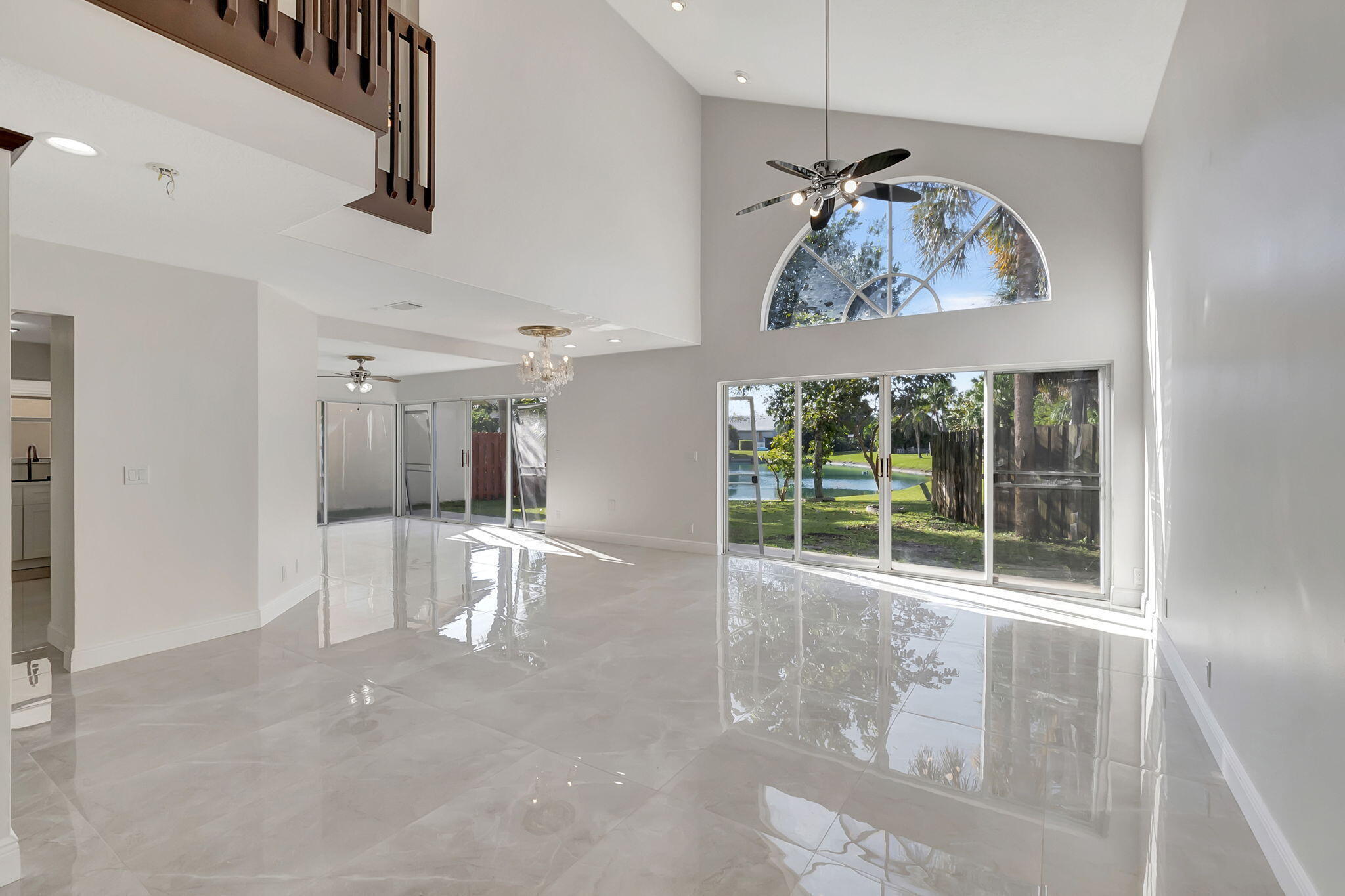 Vacant living room with glossy tile floors, an arched window, and sliding doors overlooking a waterfront yard.