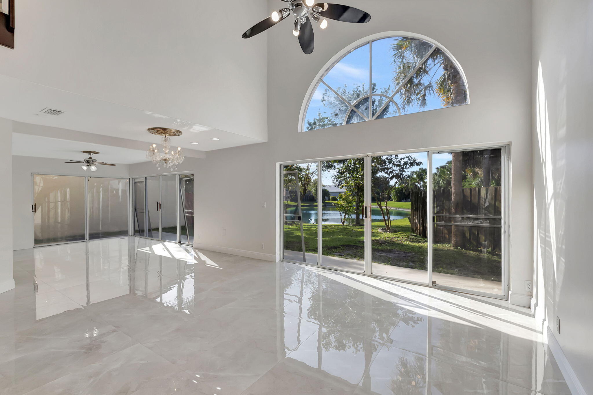 Bright vacant living room with glossy tile floors, an arched window, and sliding doors overlooking a pond.