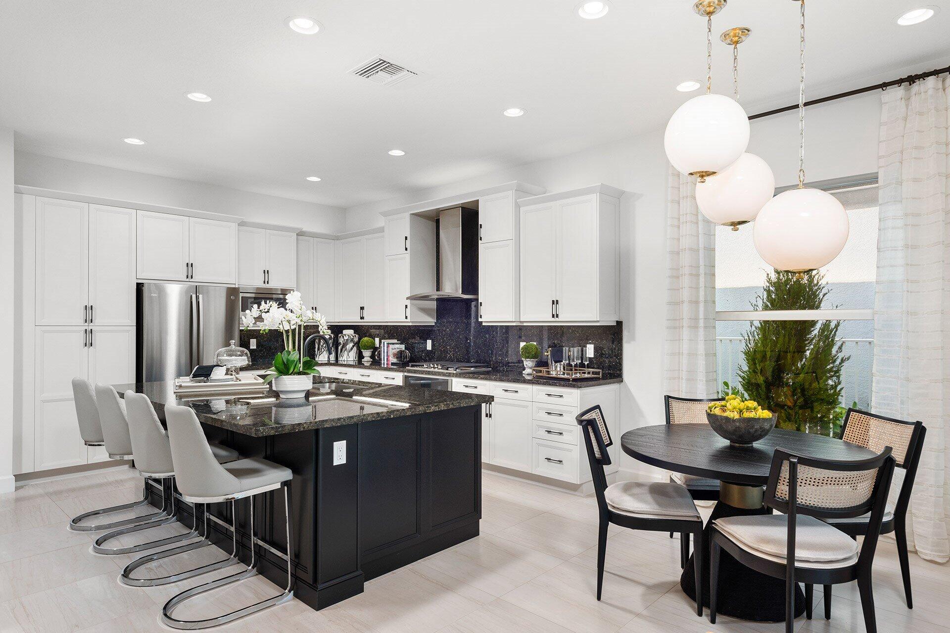 Kitchen with a dark island, white bar stools, white cabinetry, and an adjoining dining area.