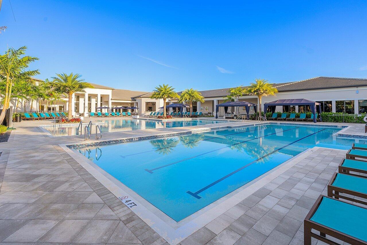 Outdoor lap pool with palm trees, tiled deck, lounge chairs, and shaded pergola seating.