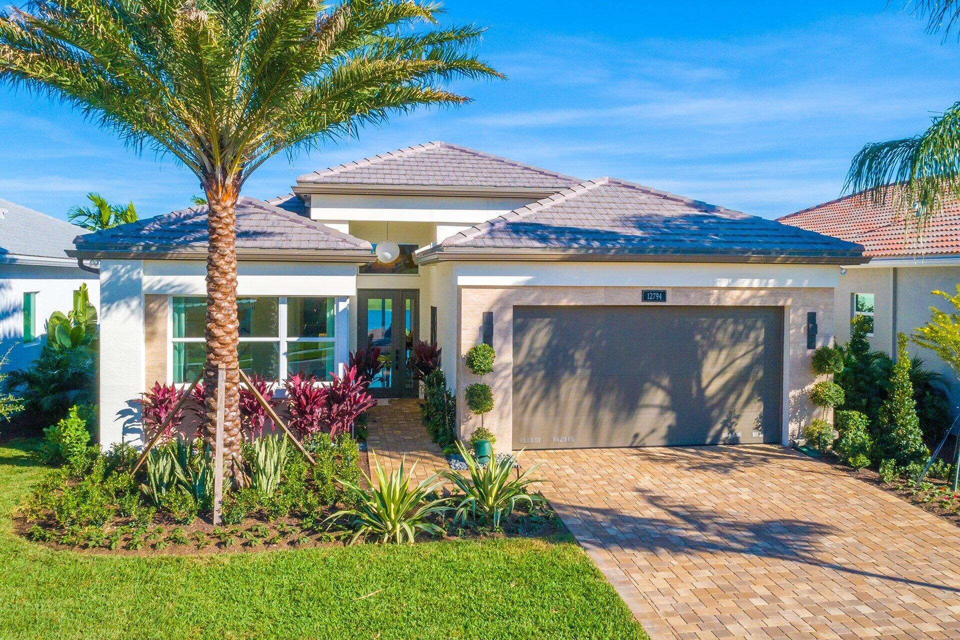Single-story home with a tiled roof, two-car garage, palm tree, and landscaped front yard.