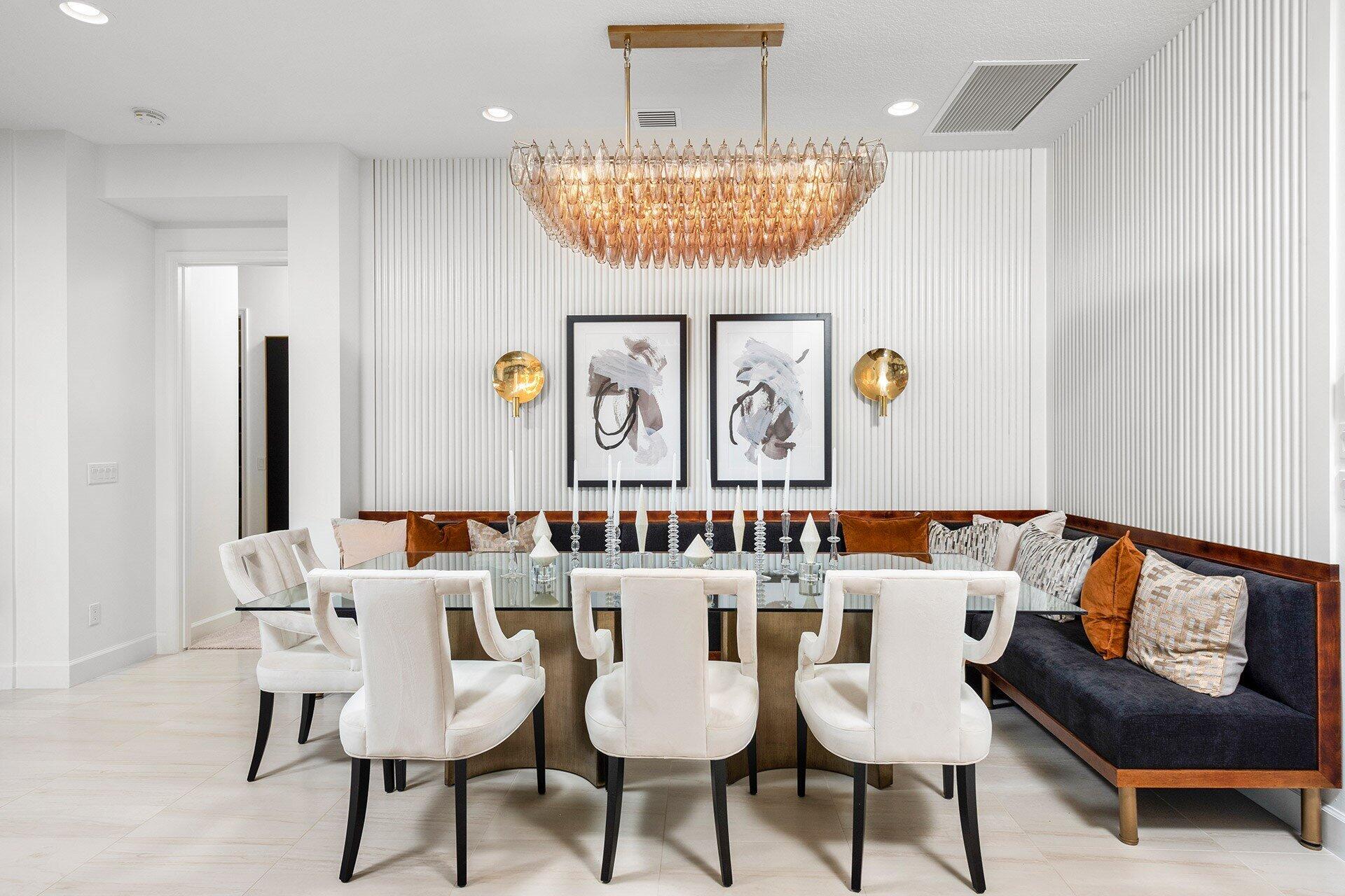 Dining room with an amber glass chandelier, glass-top table, white chairs, and built-in banquette.