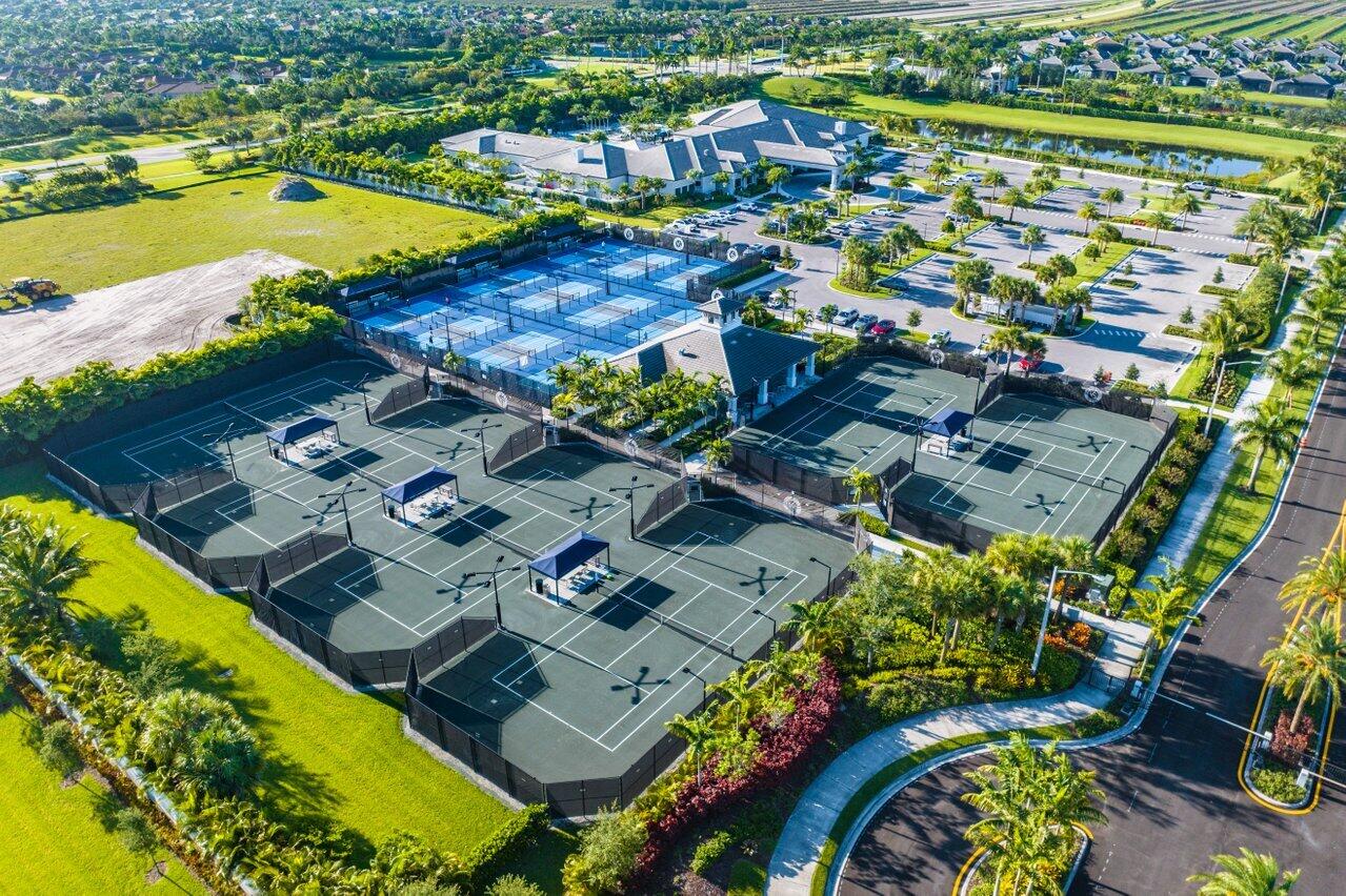 Aerial view of a community tennis complex with numerous courts, a clubhouse, and landscaped grounds.
