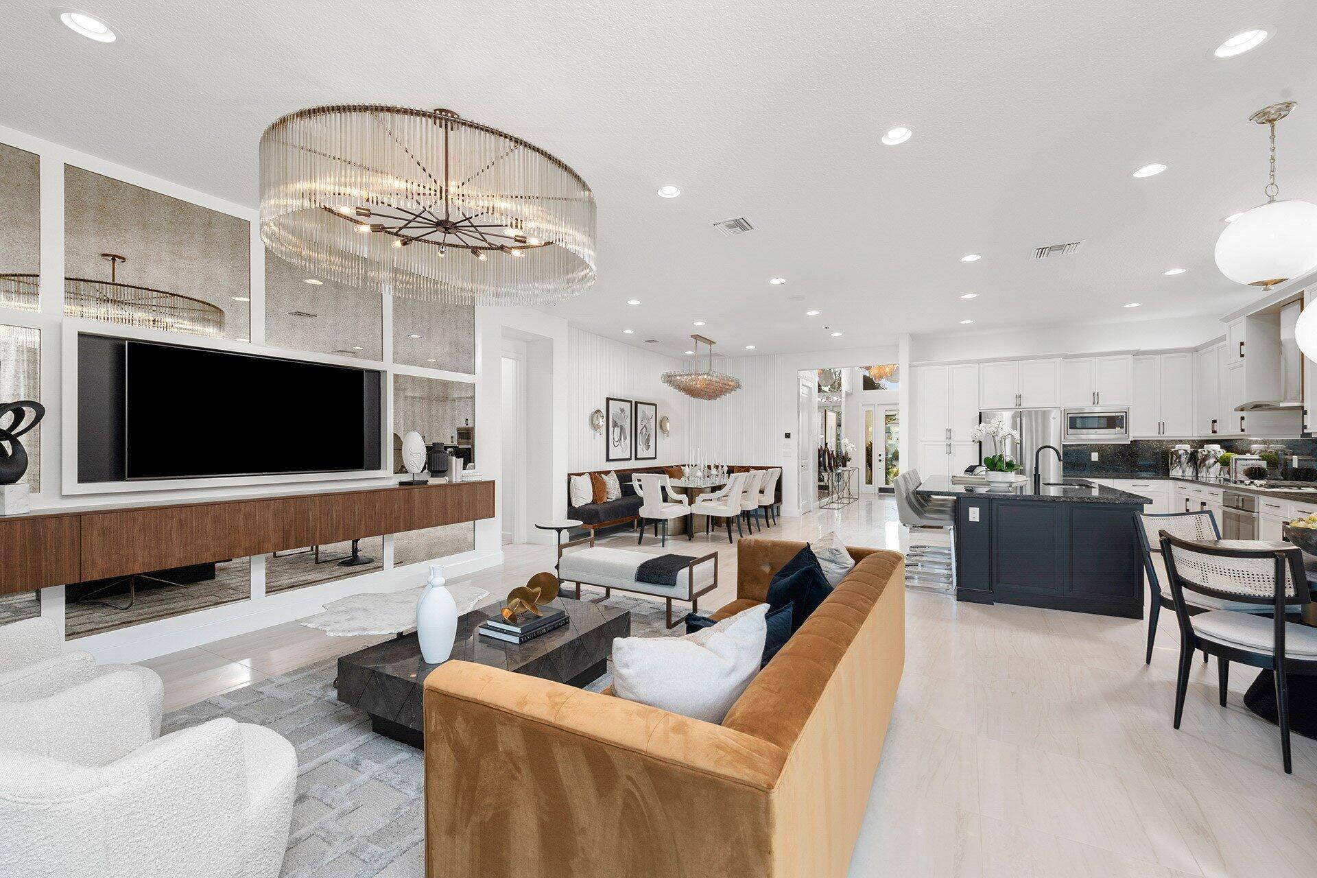 Open-plan living room, dining area, and kitchen with a statement chandelier and dark island.