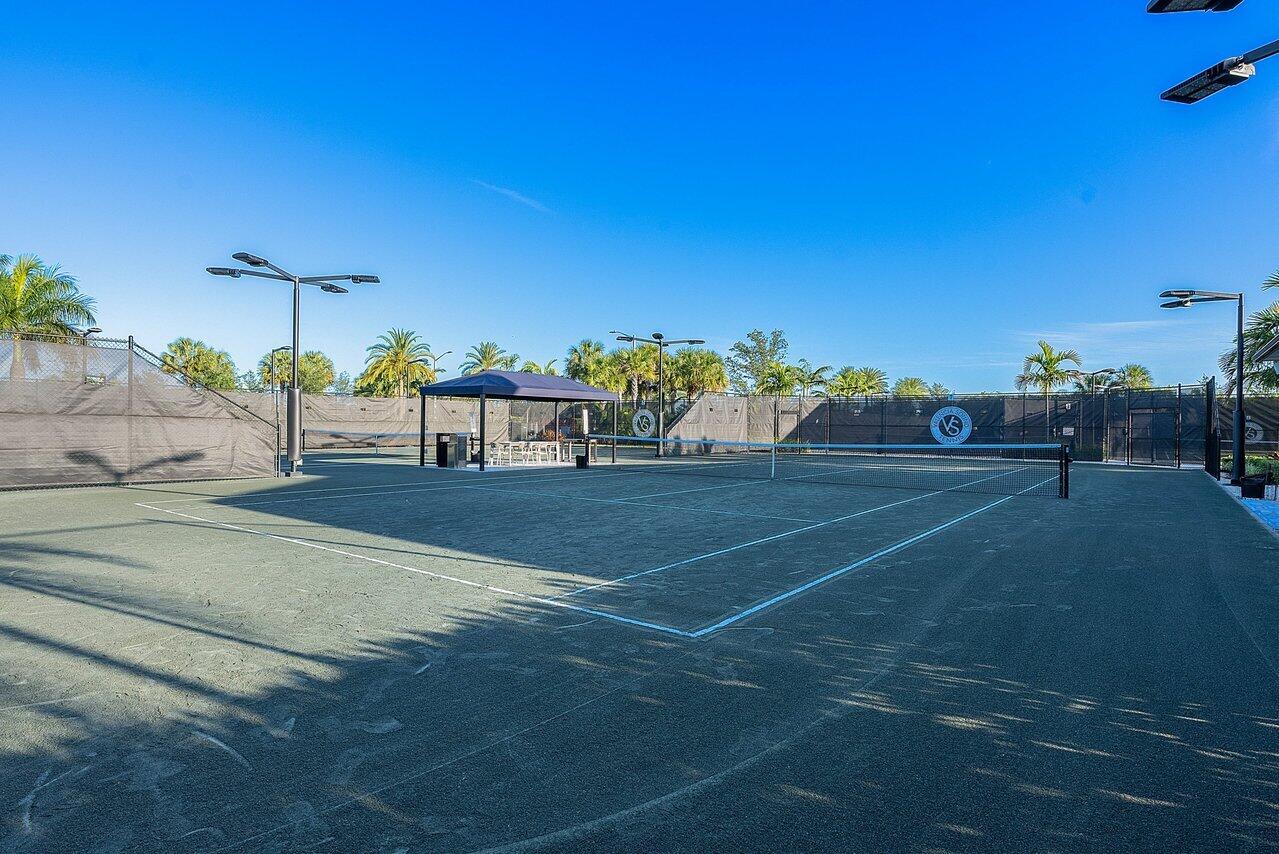 Outdoor tennis courts with fenced playing areas, palm trees and a shaded seating area.
