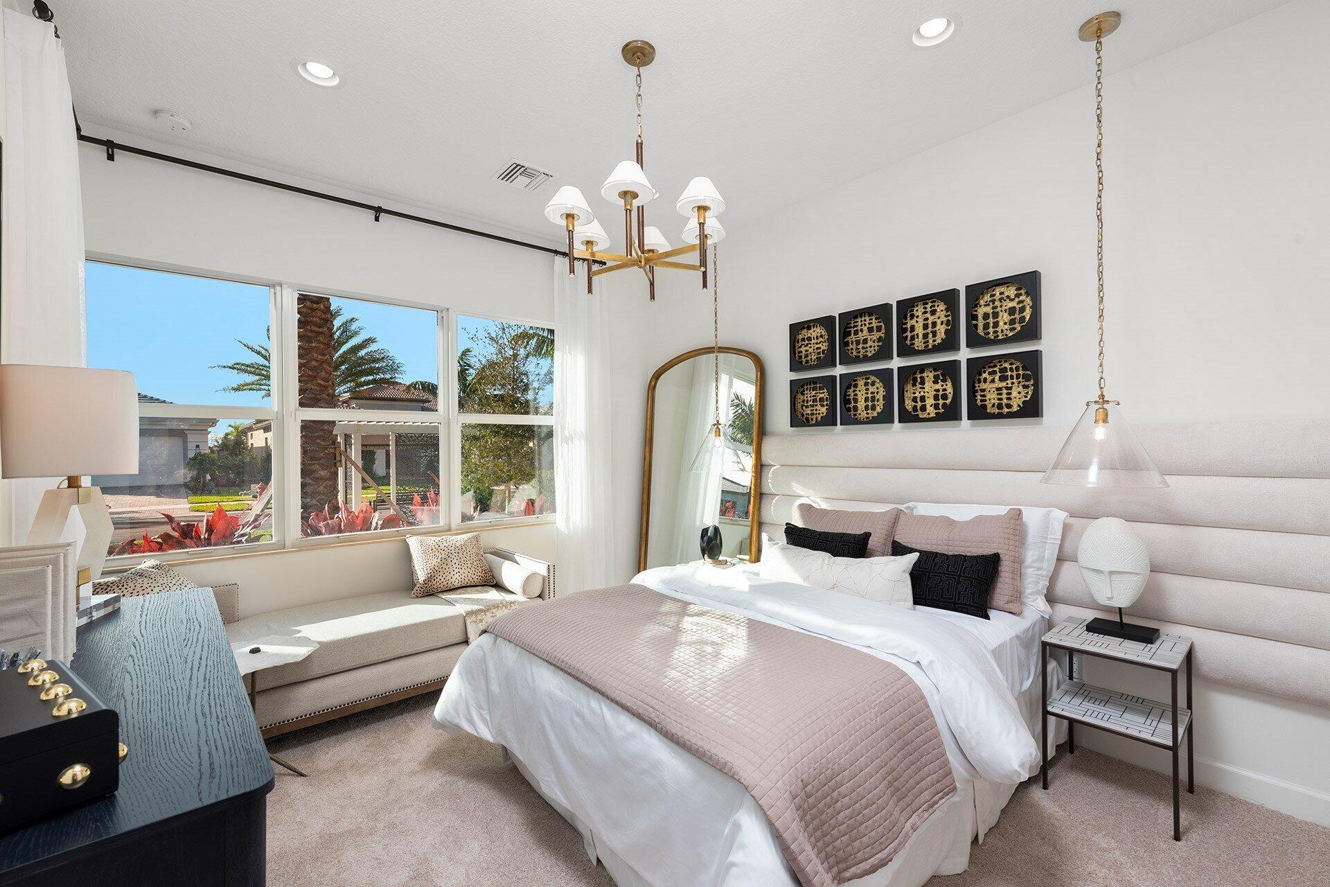Bright bedroom with blush bedding, a window-side bench, and large windows overlooking the yard.