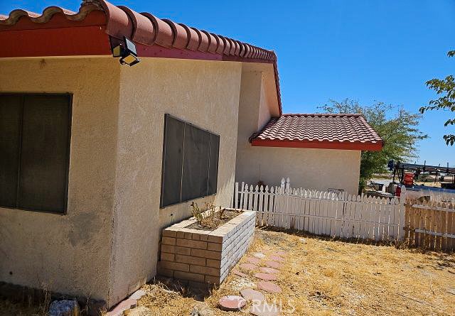 Stucco home with a red tile roof, white picket fence, and dry yard.