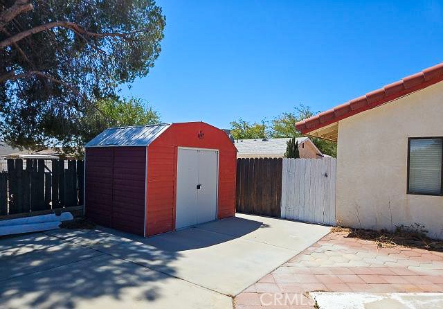 Backyard patio with a red storage shed, fenced yard, and shade tree.