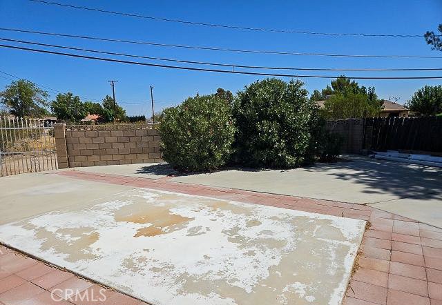 Paved yard with a weathered concrete patio, red paver border, shrubs, and block walls.