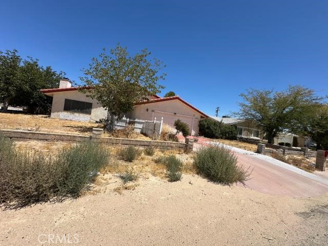 Single-story stucco house with a red tile roof, sandy yard, and paved driveway.