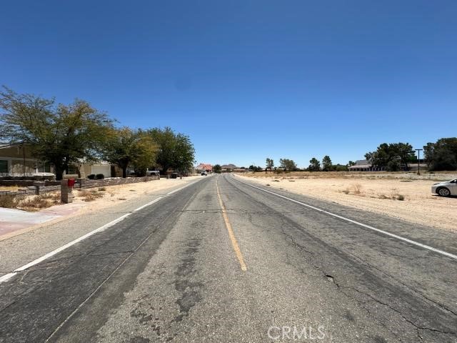 Paved road bordered by dry open lots and scattered buildings in a sparse California neighborhood.