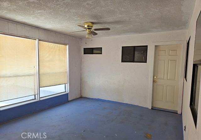 Vacant room with blue carpet, large windows with blinds, and a ceiling fan.