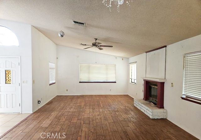 Vacant living room with wood plank flooring and a red fireplace with tiled hearth.