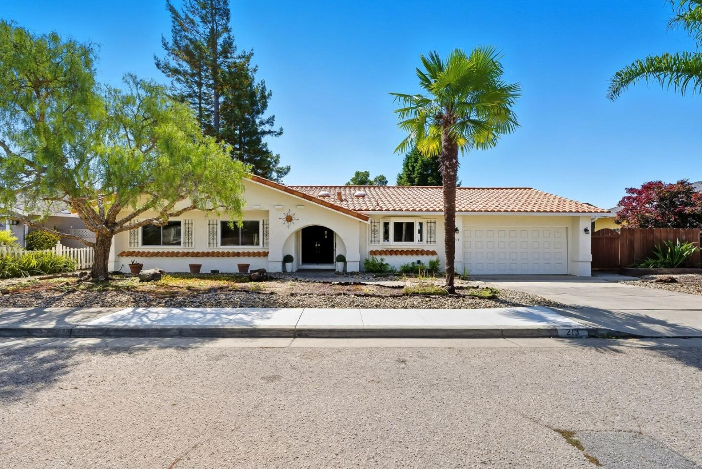 White stucco home with a tiled roof, arched entry, attached garage, and palm tree in the front yard.