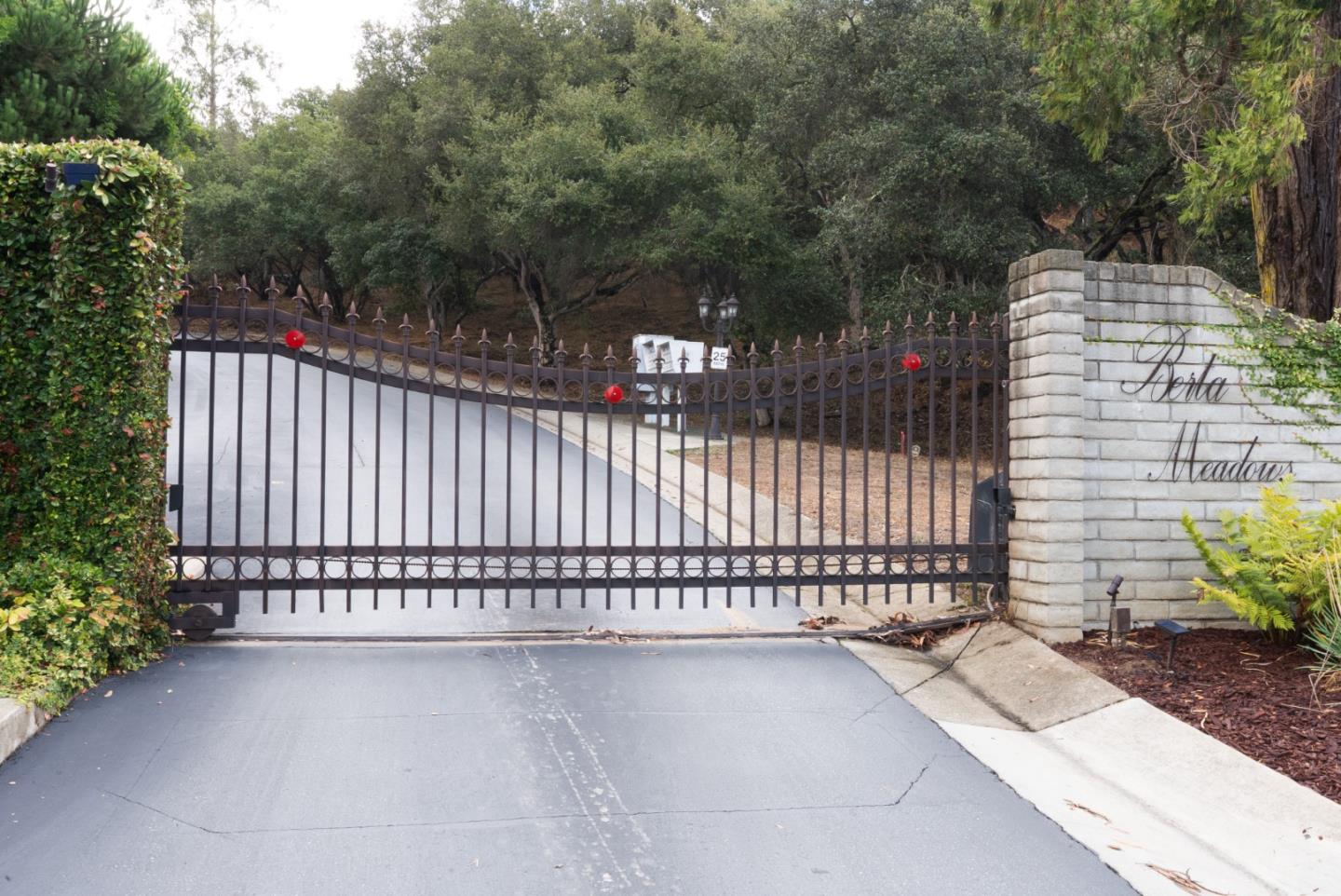 Gated Berta Meadows entrance with a wrought-iron gate, stone name wall, and wooded driveway.