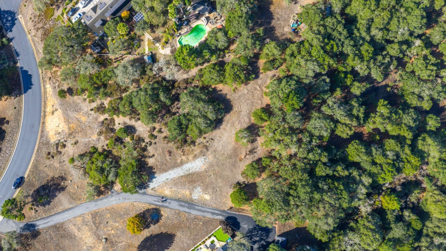 Aerial view of a wooded property with a broad clearing and paved road access.