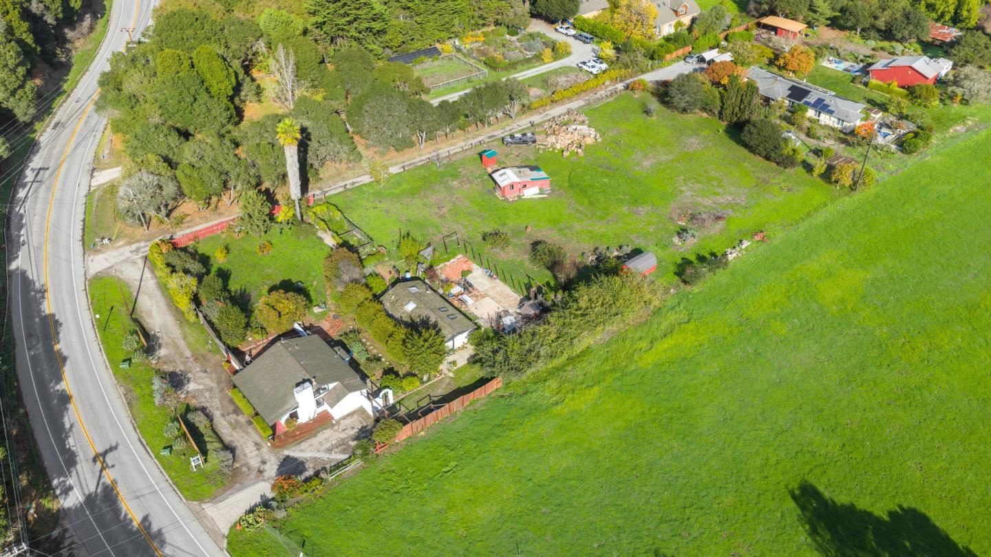 Aerial view of a rural property with several buildings beside a broad green field and paved road.