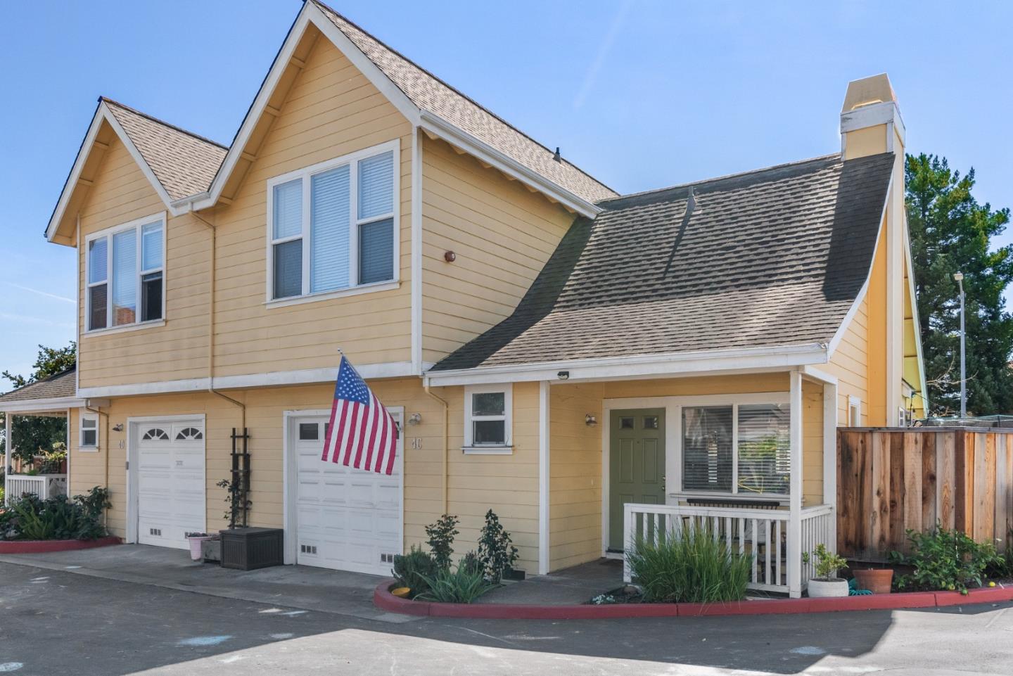 Yellow two-story home with multiple gables, a covered porch, and an American flag.