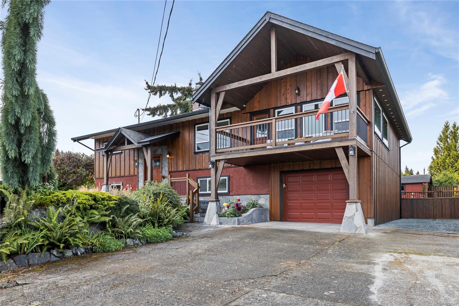 Wood-sided home with a covered upper balcony, red garage door, and landscaped driveway.